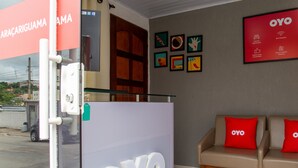Un espace d’accueil doté d’une porte en verre, d’un canapé avec des coussins rouges et d’un mur orné d’œuvres d’art encadrées, ainsi que d’un grand panneau OYO.