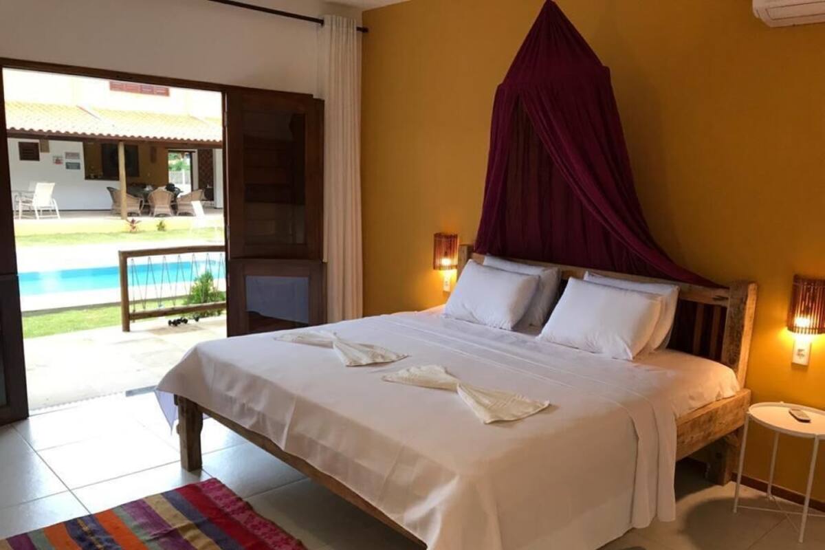 A hotel room with a bed, a view of a pool, and a dining area visible through the window.