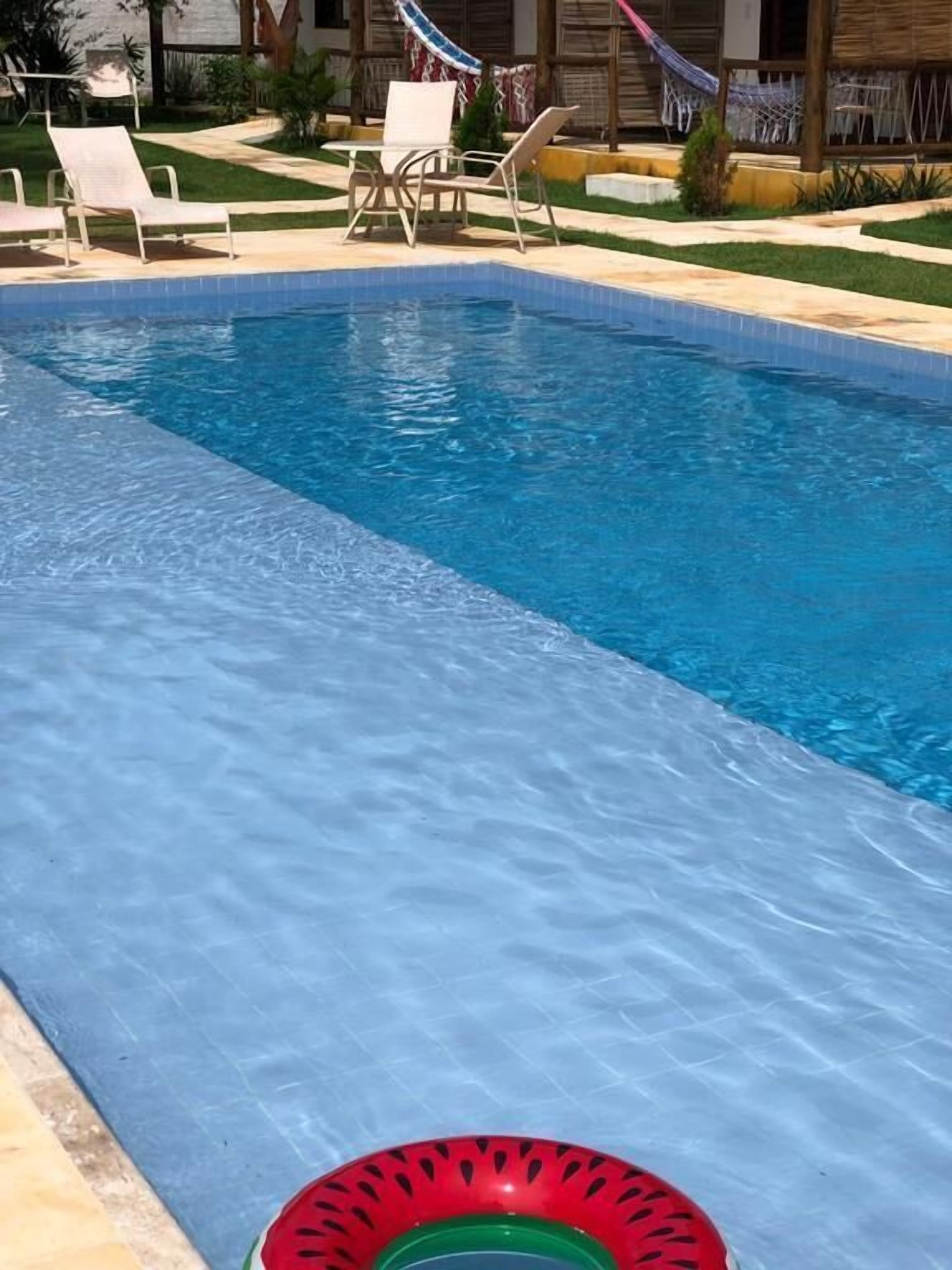 Piscina con agua azul cristalina, rodeada de sillones de descanso y una pequeña mesa.