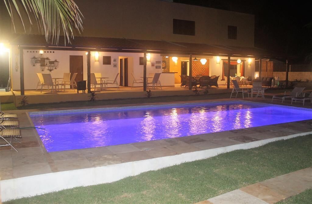 A swimming pool with a blue light, surrounded by lounge chairs and a building with outdoor seating.