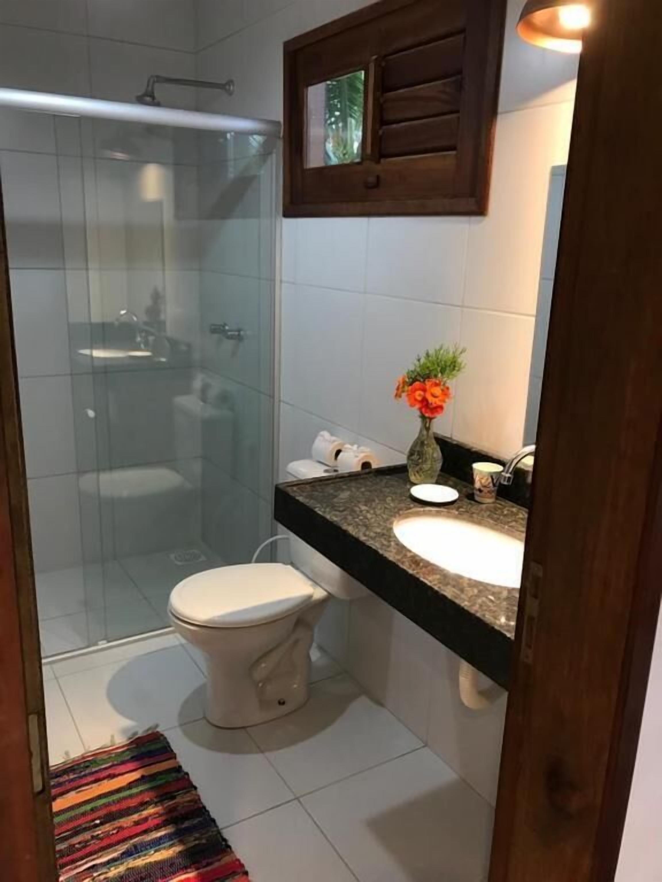 A bathroom with a glass shower enclosure, a toilet, a sink with a vase of flowers, and a wooden cabinet above the sink.