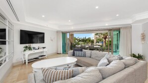 A modern living room with a large sectional sofa, a white coffee table, and a flat-screen TV mounted on the wall. - Unit 41 -  3 Bed Garden View (TERRIGAL)