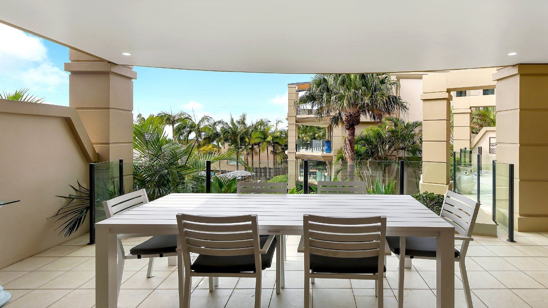 A dining area with a table and chairs, a view of a residential building, and a balcony with plants.