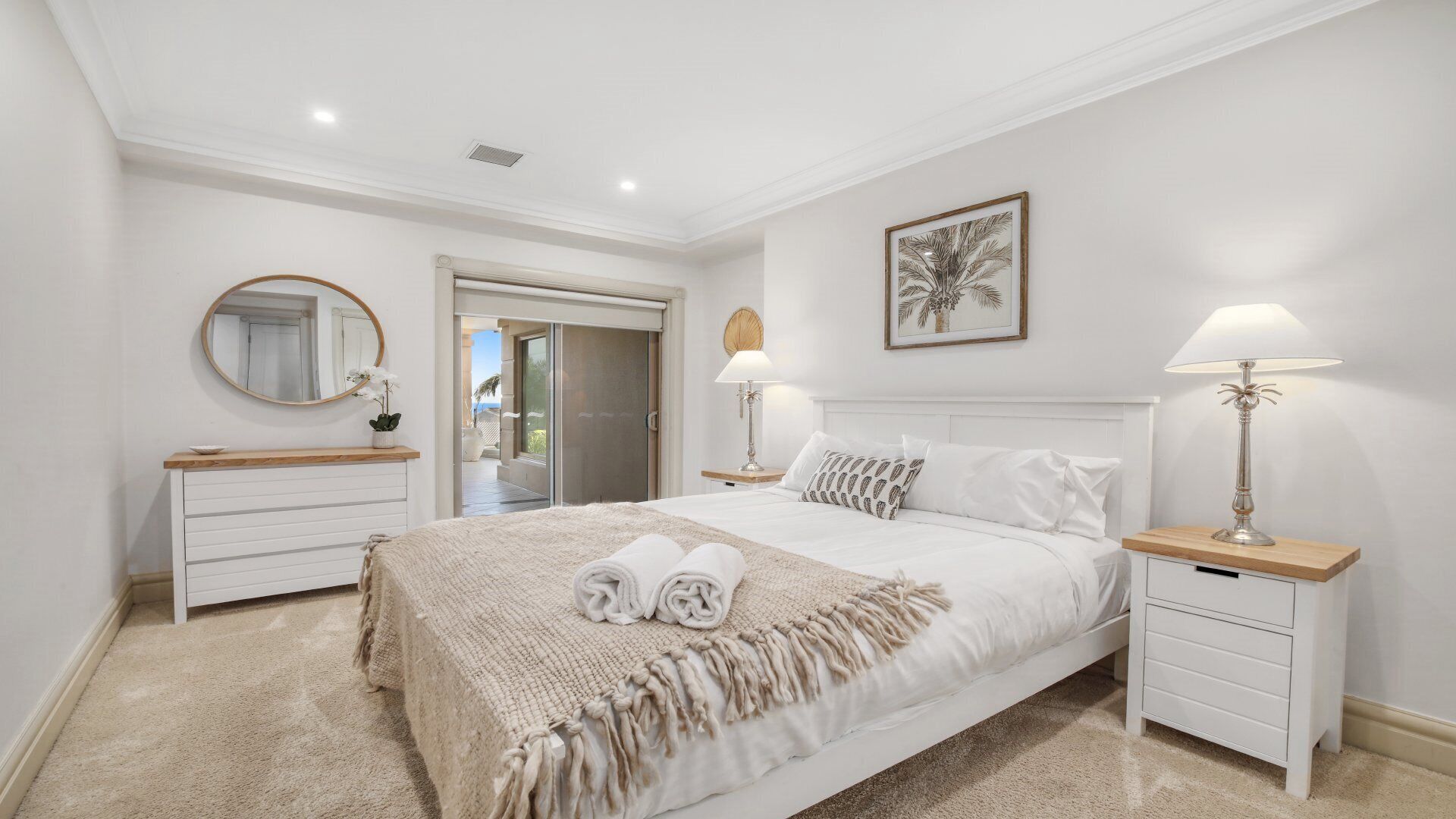 A bedroom with a bed, bedside tables, a dresser, a mirror, a door, and a framed picture on the wall.