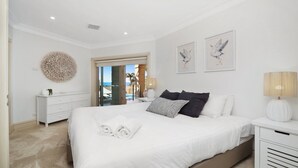A bedroom with a large bed, a dresser, a lamp, and artwork on the wall. - Unit 41 -  3 Bed Garden View (TERRIGAL)