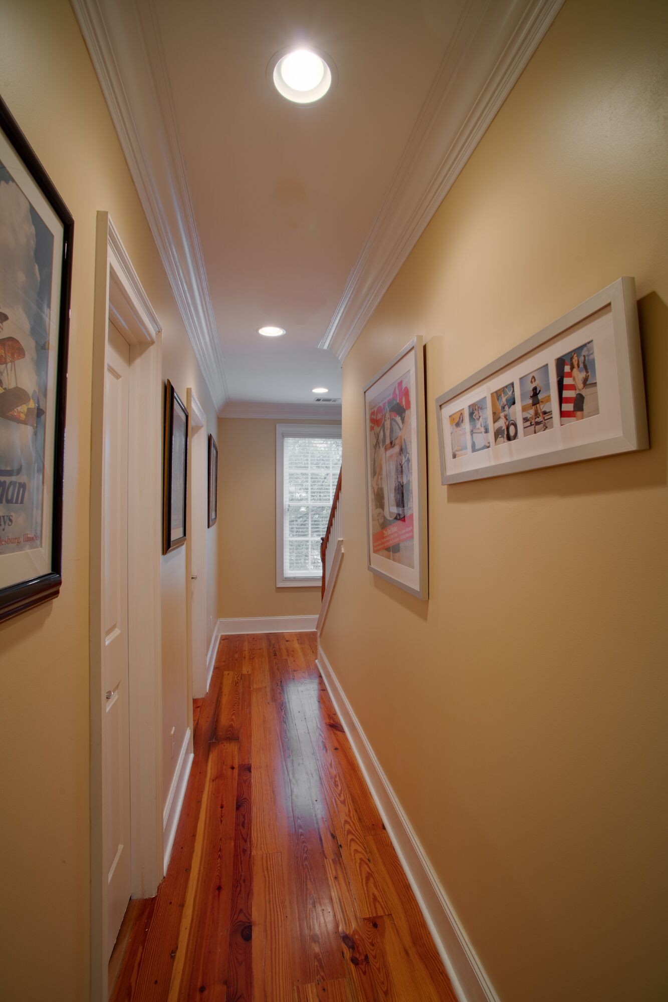 A hallway with wooden floors, cream walls, and framed pictures on the walls.
