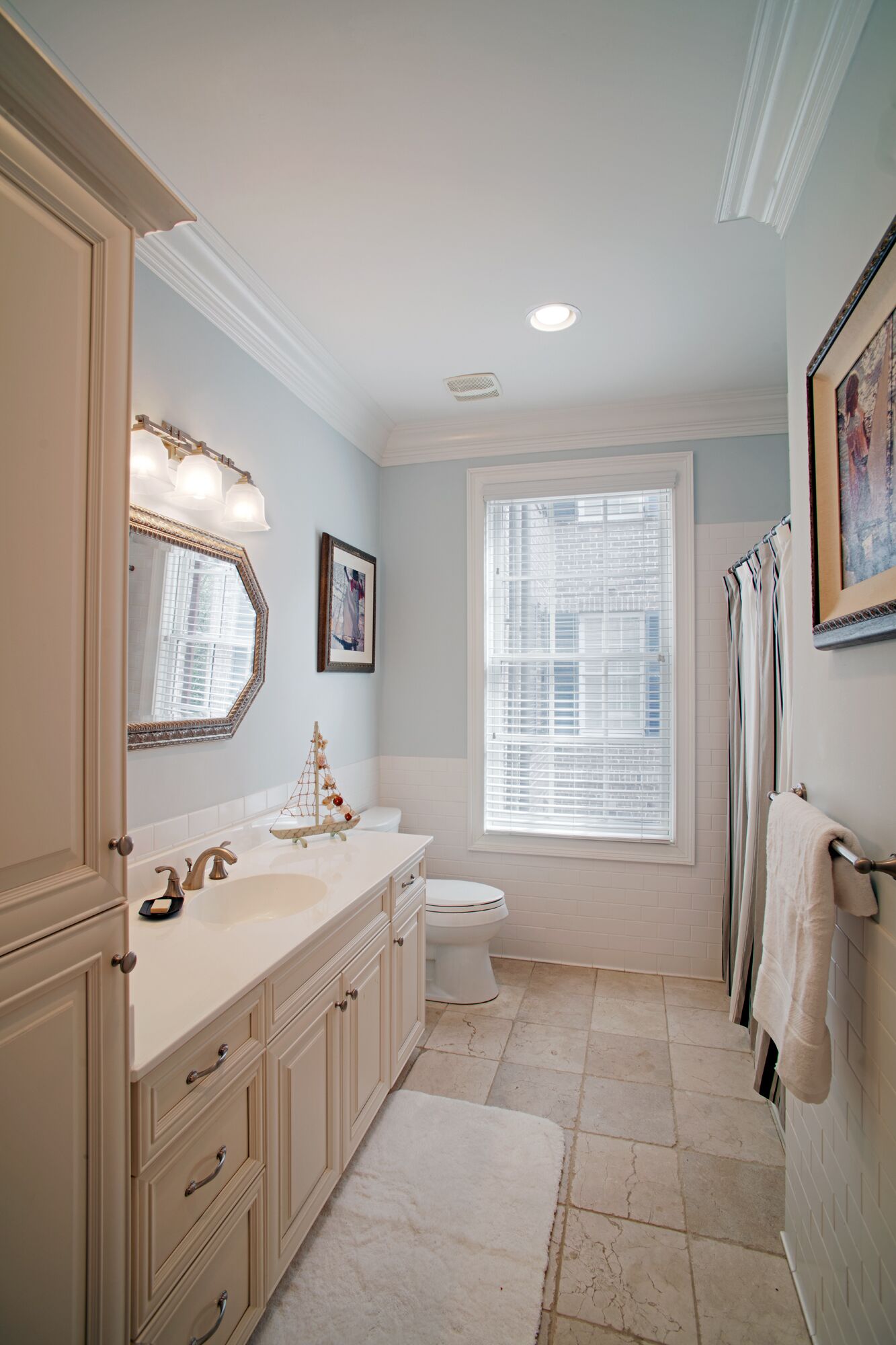 A bathroom with a double sink vanity, a toilet, a window with blinds, and a towel rack.