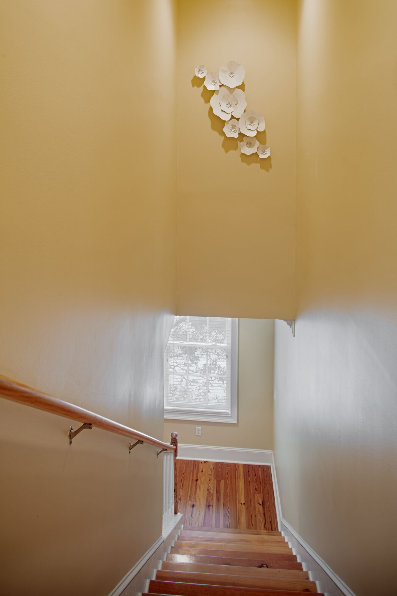 A staircase with wooden steps and a white handrail, leading to a room with a window and a wall-mounted decorative piece.