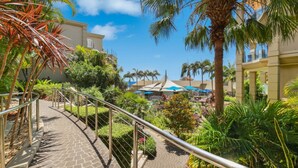 A hotel courtyard with a pool, palm trees, and outdoor seating under umbrellas. - Unit 46  - 3 Bed Ocean View (TERRIGAL)