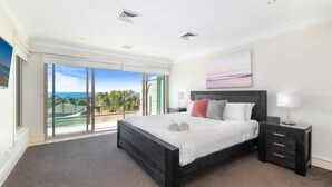 A spacious bedroom with a large bed, a nightstand, and a view of the ocean through a sliding glass door. - Unit 46  - 3 Bed Ocean View (TERRIGAL)