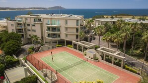 A tennis court surrounded by apartment buildings with a view of the ocean. - Unit 46  - 3 Bed Ocean View (TERRIGAL)
