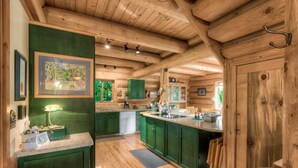 A wooden cabin interior with a kitchen area featuring green cabinets, a countertop, and a dining table. - Bonny Sky Lodge- private riverfront log cabin w/ mountain view, hot tub, generator backup! (Gold Bar)