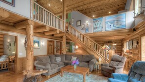 A spacious living area with a wooden staircase, a large sectional sofa, and a coffee table. - Bonny Sky Lodge- private riverfront log cabin w/ mountain view, hot tub, generator backup! (Gold Bar)