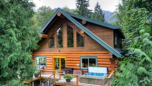 A log cabin with a deck, a hot tub, and a staircase leading to a second level. - Bonny Sky Lodge- private riverfront log cabin w/ mountain view, hot tub, generator backup! (Gold Bar)