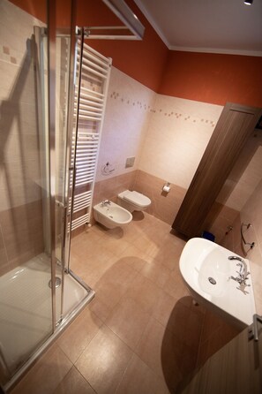 A bathroom with a glass shower enclosure, a bidet, a toilet, and a sink.