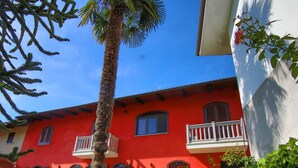 Ein rotes Gebäude mit einem Balkon, einer Palme und einem gepflegten Rasen.