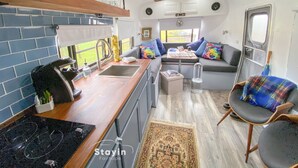 Un intérieur de camping-car compact comprenant un coin cuisine, un espace salon avec un canapé et des fauteuils, et un petit tapis.