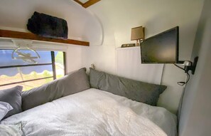 A bed with a white duvet, grey pillows, and a mounted TV on the wall.