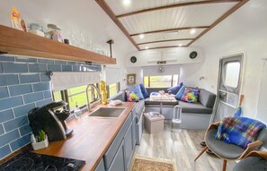 A compact RV interior with a kitchenette, a seating area with a sofa and chairs, and a small rug.