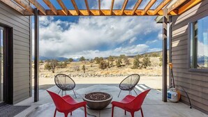 Une terrasse couverte avec un foyer, deux chaises rouges et une vue sur un paysage montagneux.