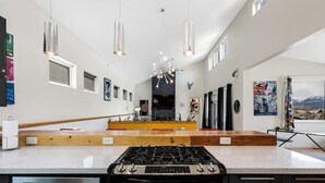 Une cuisine moderne dotée d’un îlot central, d’appareils électroménagers en acier inoxydable, de luminaires suspendus et d’œuvres d’art accrochées aux murs.