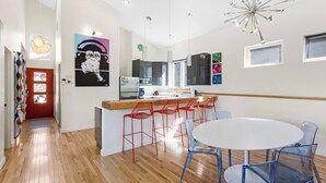 Une cuisine moderne dotée d’un îlot central, de tabourets de bar rouges et d’une table de salle à manger ronde avec des chaises bleues.