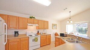A kitchen with wooden cabinets, a stove, a sink, and a window with a view. - Spacious pool home located in popular gated community of Westhaven (Davenport)