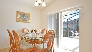A dining area with a glass table surrounded by wicker chairs, a chandelier, and a framed picture on the wall. - Spacious pool home located in popular gated community of Westhaven (Davenport)