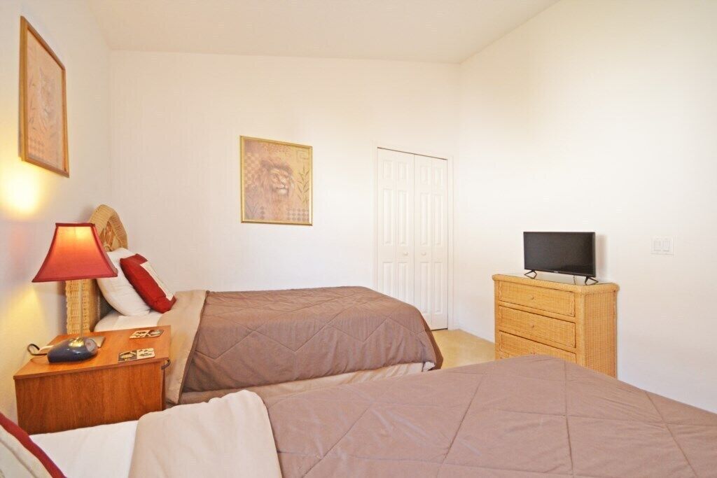 A bedroom with two beds, a bedside table with a lamp, a dresser, and a television.