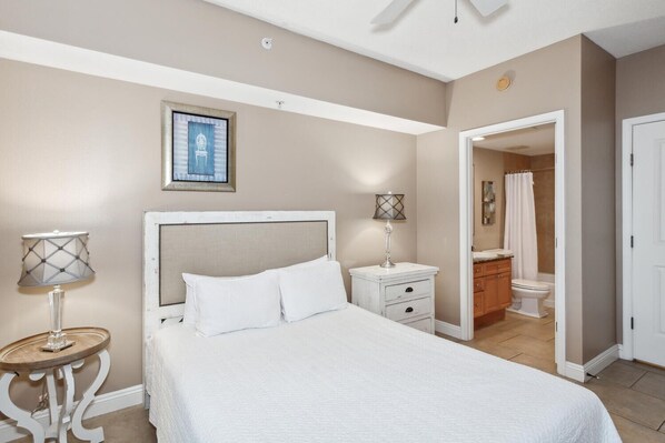 A bedroom with a bed, bedside tables, a lamp, a framed picture, and a bathroom visible through an open door.