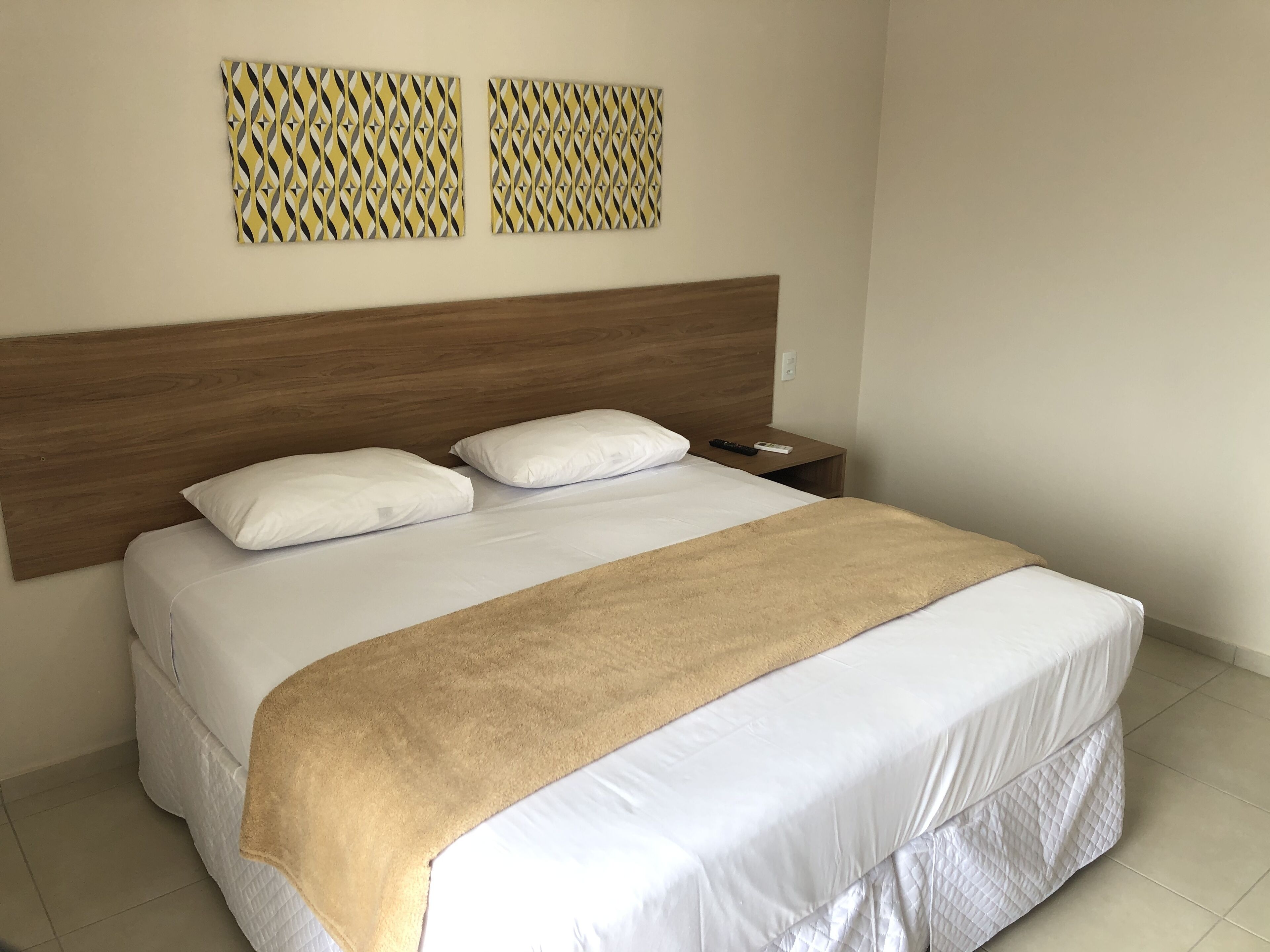 Un lit bien fait, avec une tête de lit en bois, une literie blanche et un plaid beige.