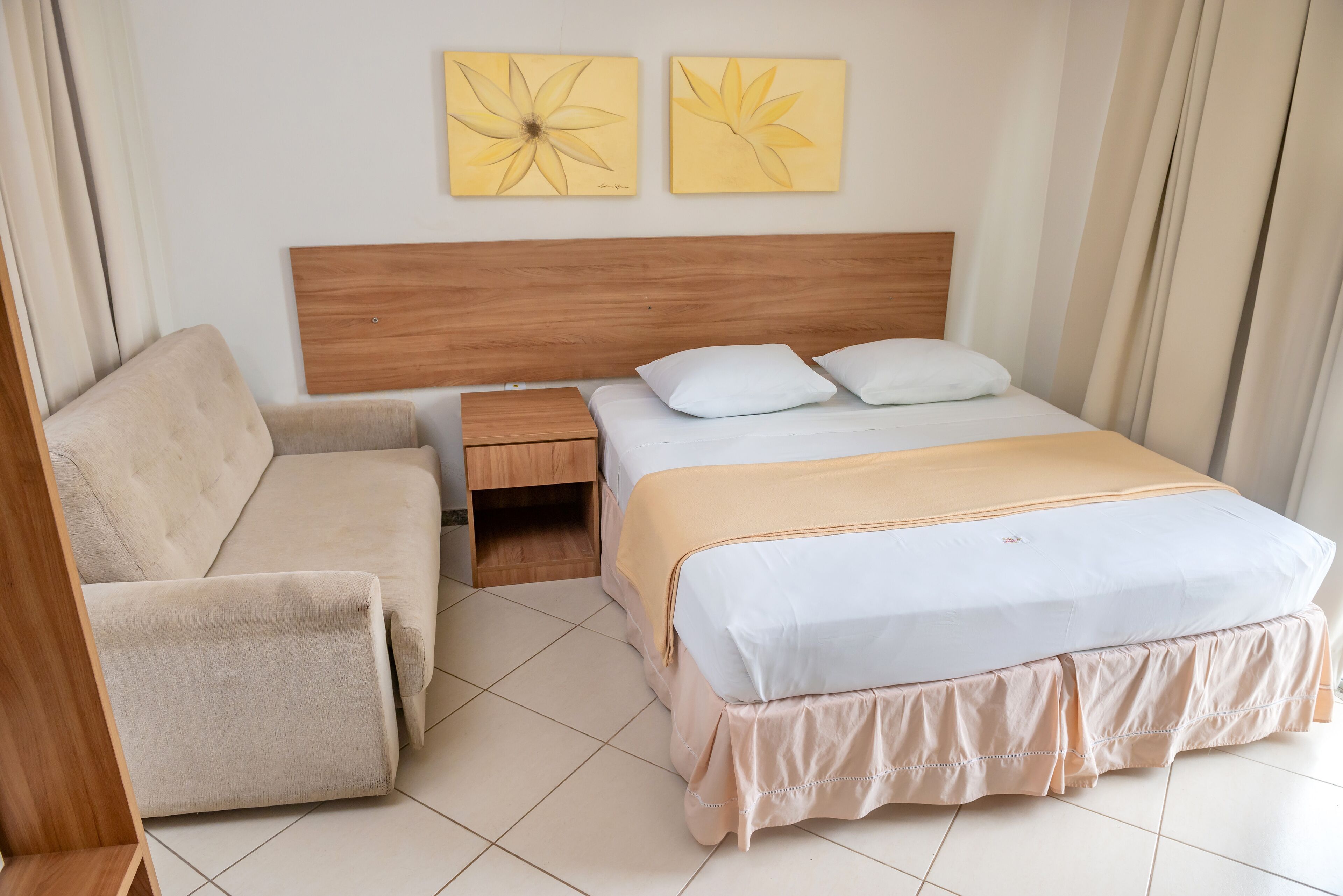 A hotel room with a bed, a sofa, a nightstand, and two wall art pieces.