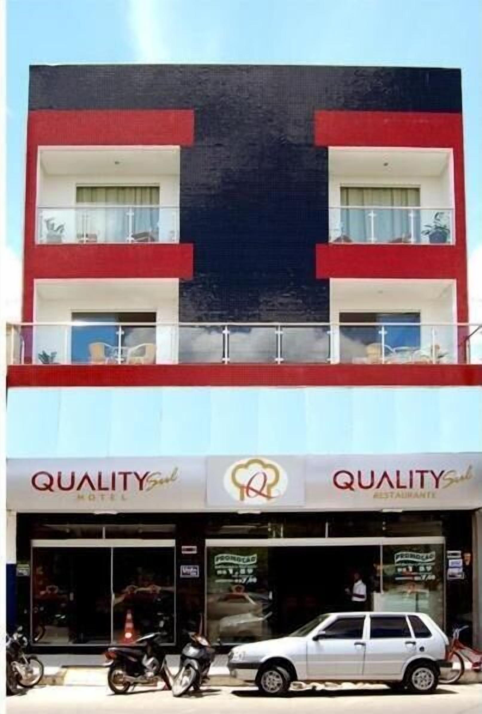 A two-story building with a red and white facade, featuring a ground-level restaurant named "QUALITY" and a visible car parked in front.