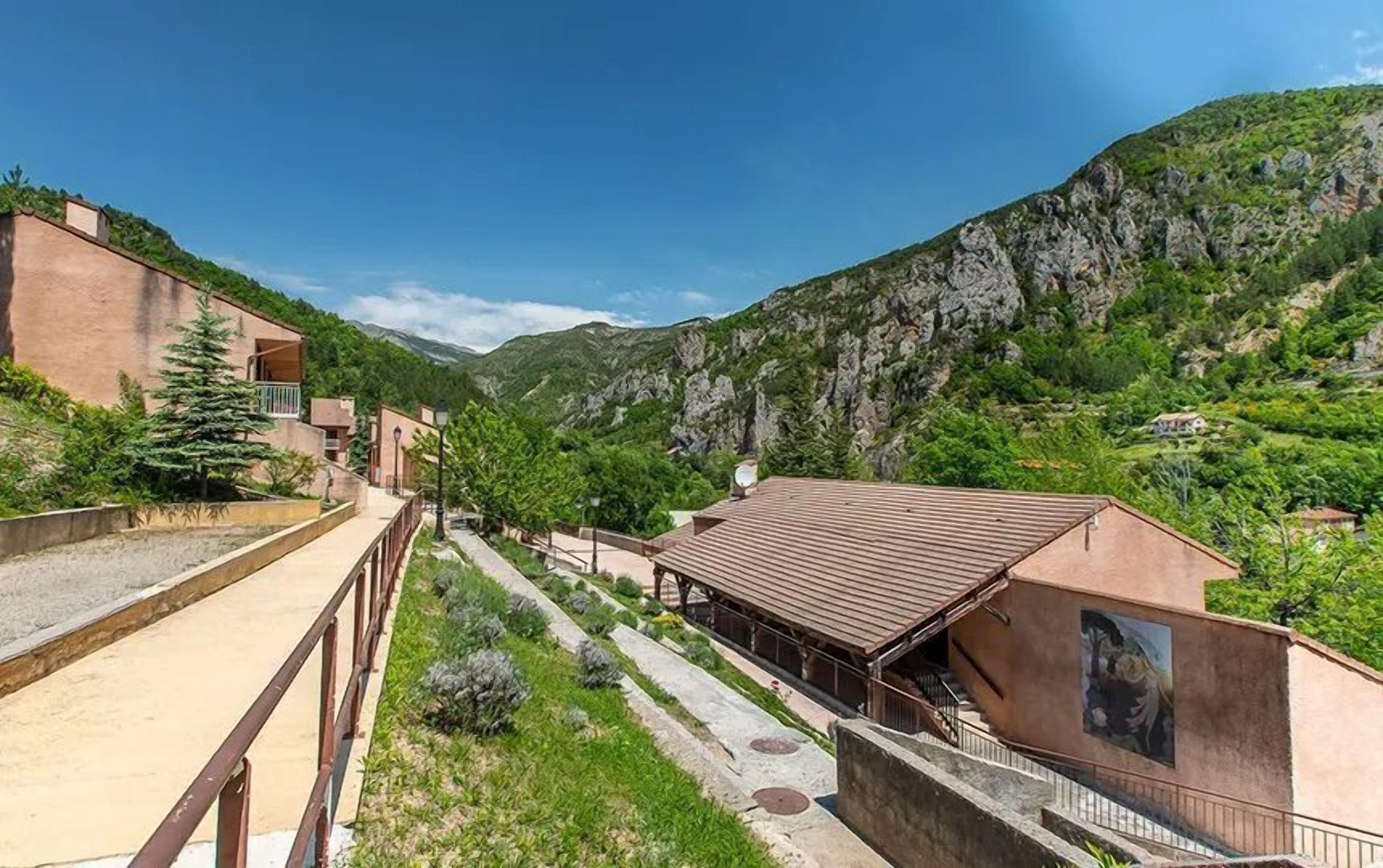 A hillside property with a building featuring a balcony, a covered patio, and a view of the surrounding mountainous landscape.