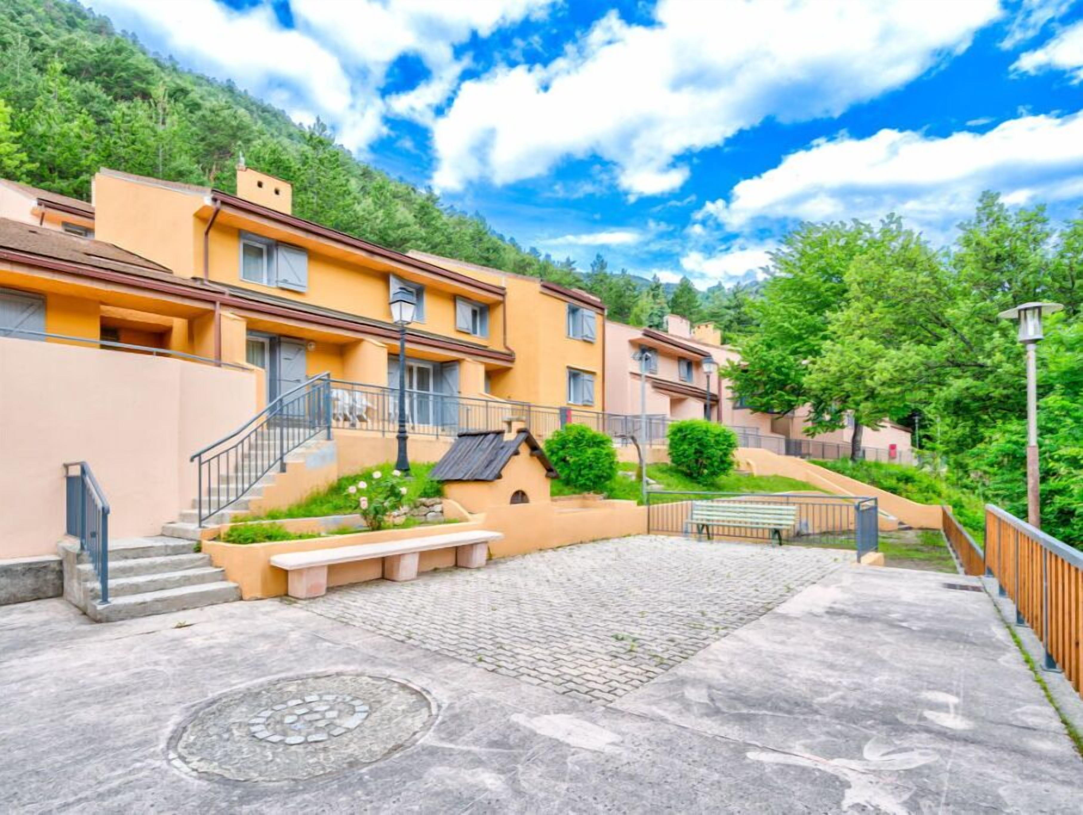 A residential building with a paved courtyard, steps leading to a balcony, and a manhole cover.