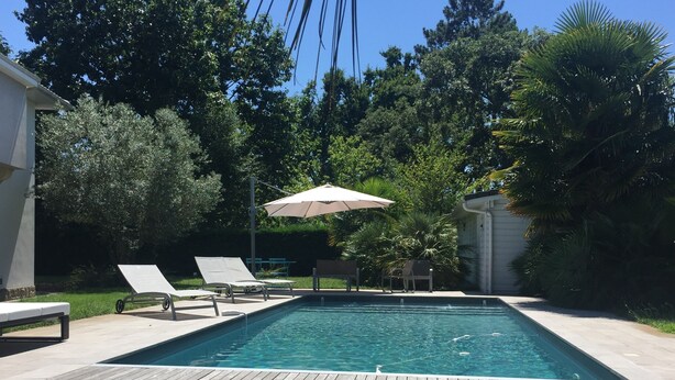 A rectangular swimming pool with a wooden deck, two lounge chairs, and a single umbrella. - House and its pool near the beach (Andernos-les-Bains)