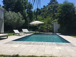 Une piscine rectangulaire avec une terrasse en bois, deux chaises longues et un seul parasol.