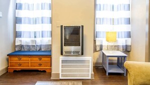 A room with a wooden dresser, a radiator, a small table with a lamp, and striped curtains. - Suite #2 - 1 Bed 1 Bath in Downtown Hermann (Hermann)
