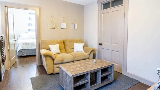 A living room with a beige sofa, a coffee table, and a door. - Suite #2 - 1 Bed 1 Bath in Downtown Hermann (Hermann)