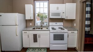 A compact kitchen with white cabinets, a built-in microwave, a stove, and a refrigerator. - Suite #2 - 1 Bed 1 Bath in Downtown Hermann (Hermann)