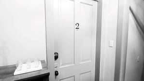 A white door with the number 2, a wooden bench with glasses, and a doorbell. - Suite #2 - 1 Bed 1 Bath in Downtown Hermann (Hermann)