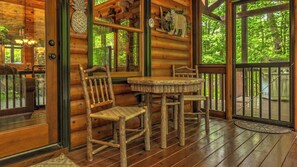 A wooden cabin interior with a dining table and chairs, a chandelier, and a large window overlooking a forest. - Our Blue Heaven- Private, yet convenient | Hot tub |Screened Porch (Blue Ridge)