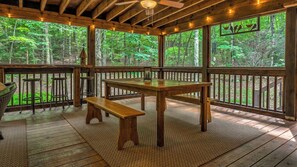 A wooden deck with a table and benches, surrounded by large windows offering a view of a forest. - Our Blue Heaven- Private, yet convenient | Hot tub |Screened Porch (Blue Ridge)