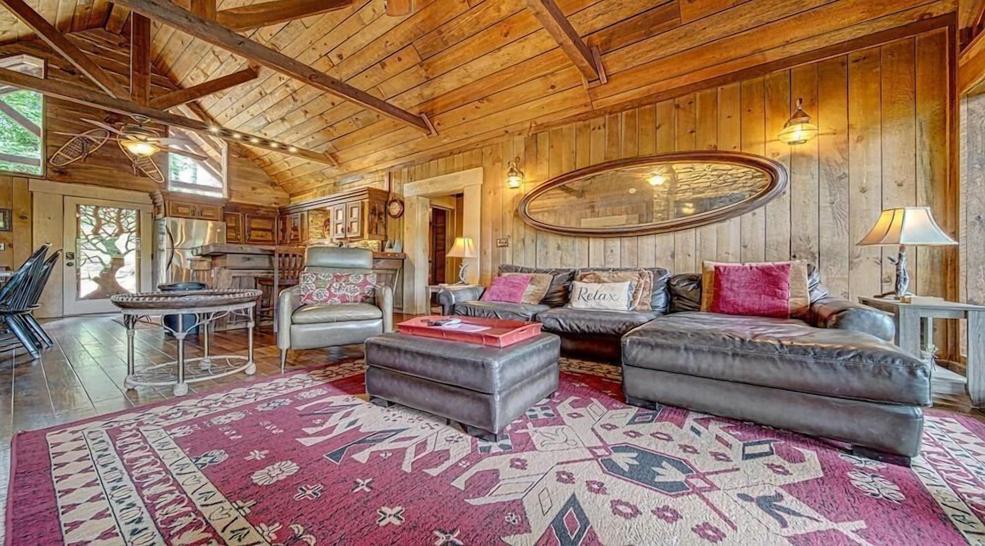 Un intérieur chaleureux et rustique, avec des poutres en bois, un grand miroir ovale, des canapés en cuir et un tapis à motifs.