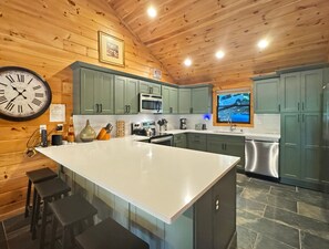 A kitchen with a central island, green cabinets, a clock, and a window with a view.