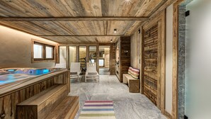 Een wellnessruimte met houten plafond, een whirlpool en een zithoek met een kleurrijk vloerkleed.