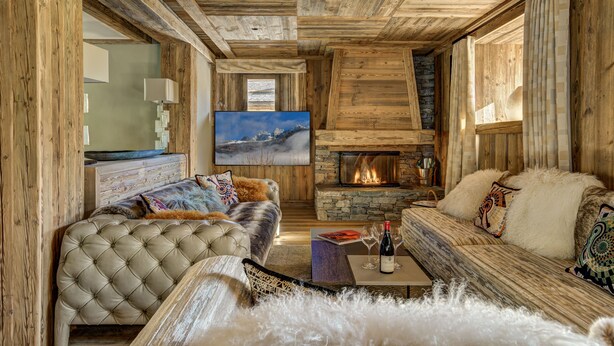 Een gezellig interieur van een blokhut met een open haard, houten wanden, een televisie en comfortabele zitmogelijkheden.