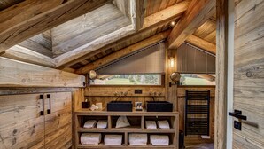Een rustiek houten interieur met een schuine plafond, houten planken met handdoeken en een raam met uitzicht op groen.