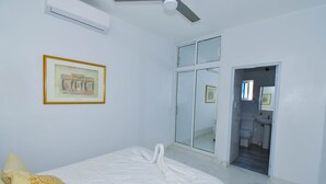 A hotel room with a bed, a ceiling fan, a framed picture on the wall, and a bathroom visible through an open door. - Rosil Place (Puerto Plata)