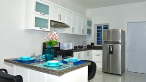 A modern kitchen with white cabinets, a stainless steel refrigerator, and a blue vase with flowers on the island. - Rosil Place (Puerto Plata)